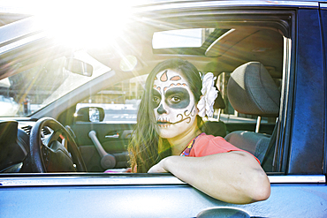 Hispanic woman driving car wearing skull face paint