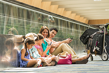 Family waiting on floor of airport using cell phones