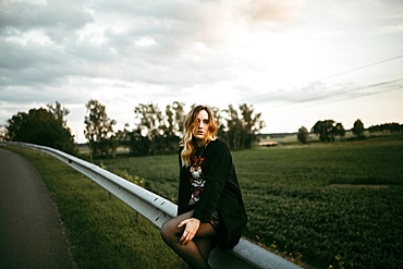 Caucasian woman sitting on guardrail near road