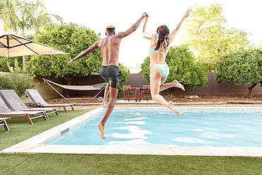 Couple holding hands jumping into swimming pool