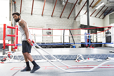 Black man pulling heavy ropes in gymnasium