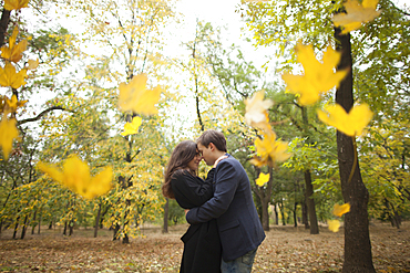 Autumn leaves falling near hugging Caucasian couple