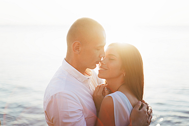 Caucasian couple hugging near ocean at sunset