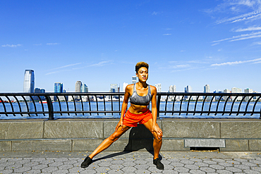 Mixed race woman stretching legs at waterfront