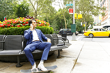 Caucasian businessman sitting on bench in city talking on cell phone