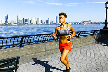 Mixed race woman running at waterfront listening to earbuds