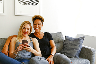 Women sitting on sofa texting on cell phone