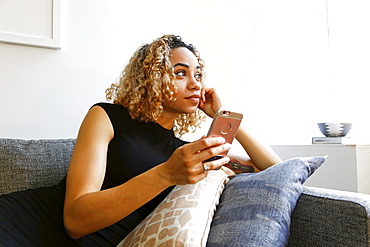 Mixed race woman laying on sofa holding cell phone