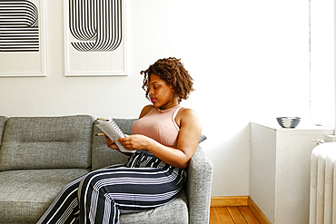 Mixed race woman reading notebook on sofa