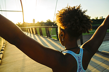 Mixed Race woman wearing earbuds stretching arms on bridge