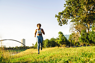 Mixed Race woman running in grass near waterfront