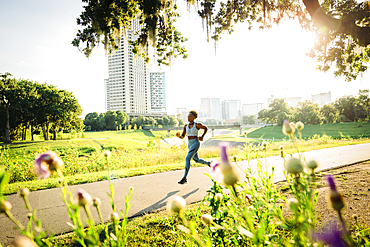 Mixed Race woman running on path in park beyond wildflowers