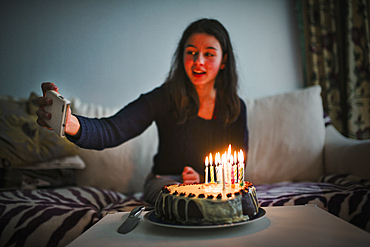 Mixed race girl posing for cell phone selfie with birthday cake