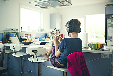 Mixed race boy sitting in kitchen listening to cell phone