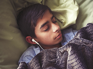 Mixed race boy laying in bed listening to earbuds