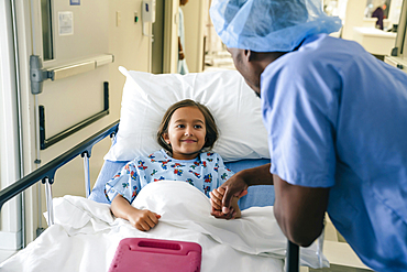 Doctor holding hand of girl in hospital bed