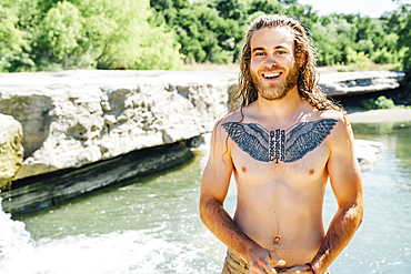 Smiling Caucasian man with chest tattoo standing near river