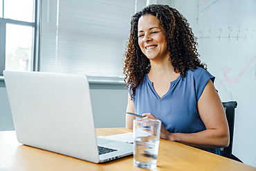 Mixed race businesswoman smiling at laptop