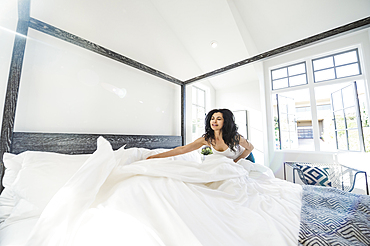 Hispanic woman arranging comforter on bed