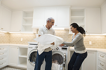 Playful couple folding towel in modern laundry room