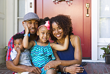 Portrait of smiling mixed race family sitting on front stoop