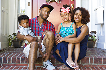 Portrait of smiling mixed race family sitting on front stoop