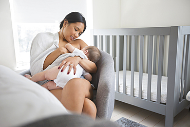 Woman sitting in armchair breast-feeding baby son