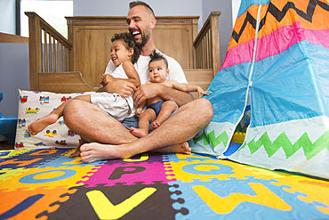 Father sitting on floor of playroom holding son and daughter