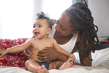 Mother holding smiling baby daughter on bed