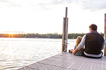 Caucasian father and daughter sitting on pier at sunset