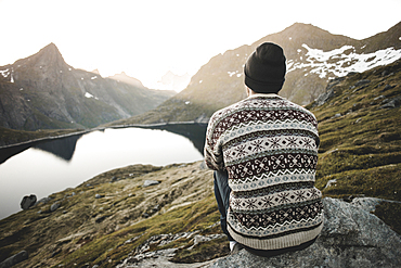 Caucasian man sitting on rock admiring scenic view of mountain lake