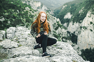 Portrait of smiling Caucasian woman sitting on rock holding camera