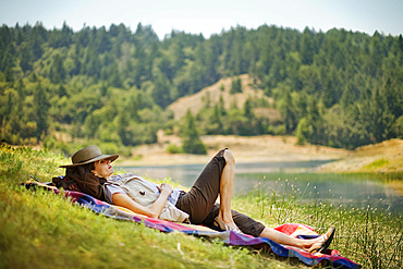 Hispanic woman relaxing on blanket near river