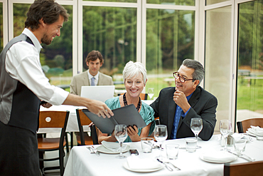 Waiter presenting menu to couple in restaurant