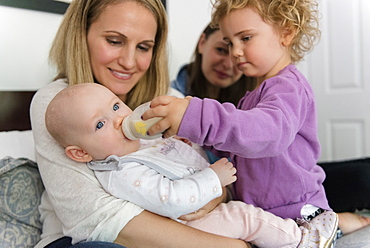 Caucasian girl feeding bottle to baby sister