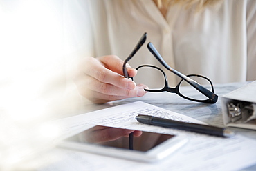 Hands of Caucasian woman holding eyeglasses near pen and cell phone