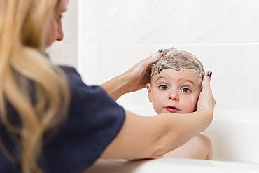 Caucasian mother washing hair of girl in bathtub