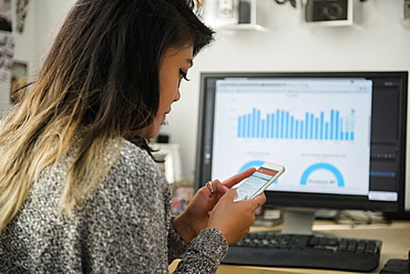 Mixed Race woman texting on cell phone near computer