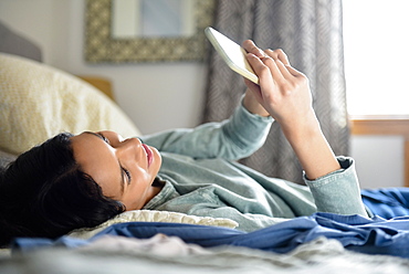 Hispanic woman laying in bed texting on cell phone