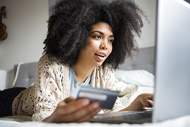 African American woman laying in bed online shopping with laptop