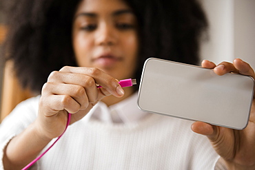 African American woman connecting cable to cell phone