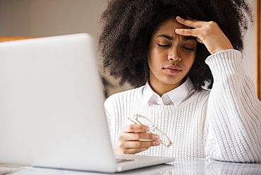 Frustrated African American woman holding eyeglasses near laptop