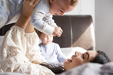 Caucasian mother laying on bed lifting baby son