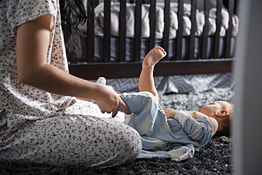 Caucasian mother dressing baby son on floor