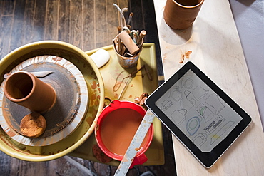 Cup and tools on pottery wheel near digital tablet