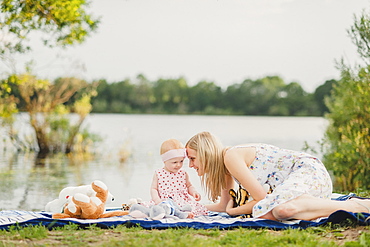 Mother and daughter playing with stuffed animals on blanket near lake