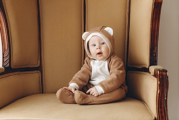 Caucasian baby boy sitting in armchair wearing bear costume