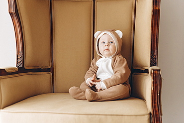 Caucasian baby boy sitting in armchair wearing bear costume