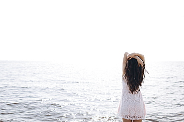 Woman standing near ocean with arms raised