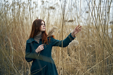 Caucasian woman standing in field touching stalk of grass